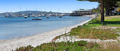 Un puerto costero con barcos amarrados, una playa de arena y un edificio con techo verde.