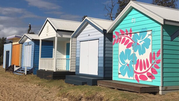 Una hilera de cabañas de playa con diferentes colores y diseños, cada una con un estilo arquitectónico propio.