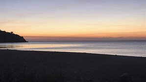 Una playa con mar en calma y cielo despejado durante la puesta de sol.
