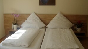 Een tweepersoonsbed met witte lakens, een houten hoofdbord en een klein nachtkastje met een potorkidee.