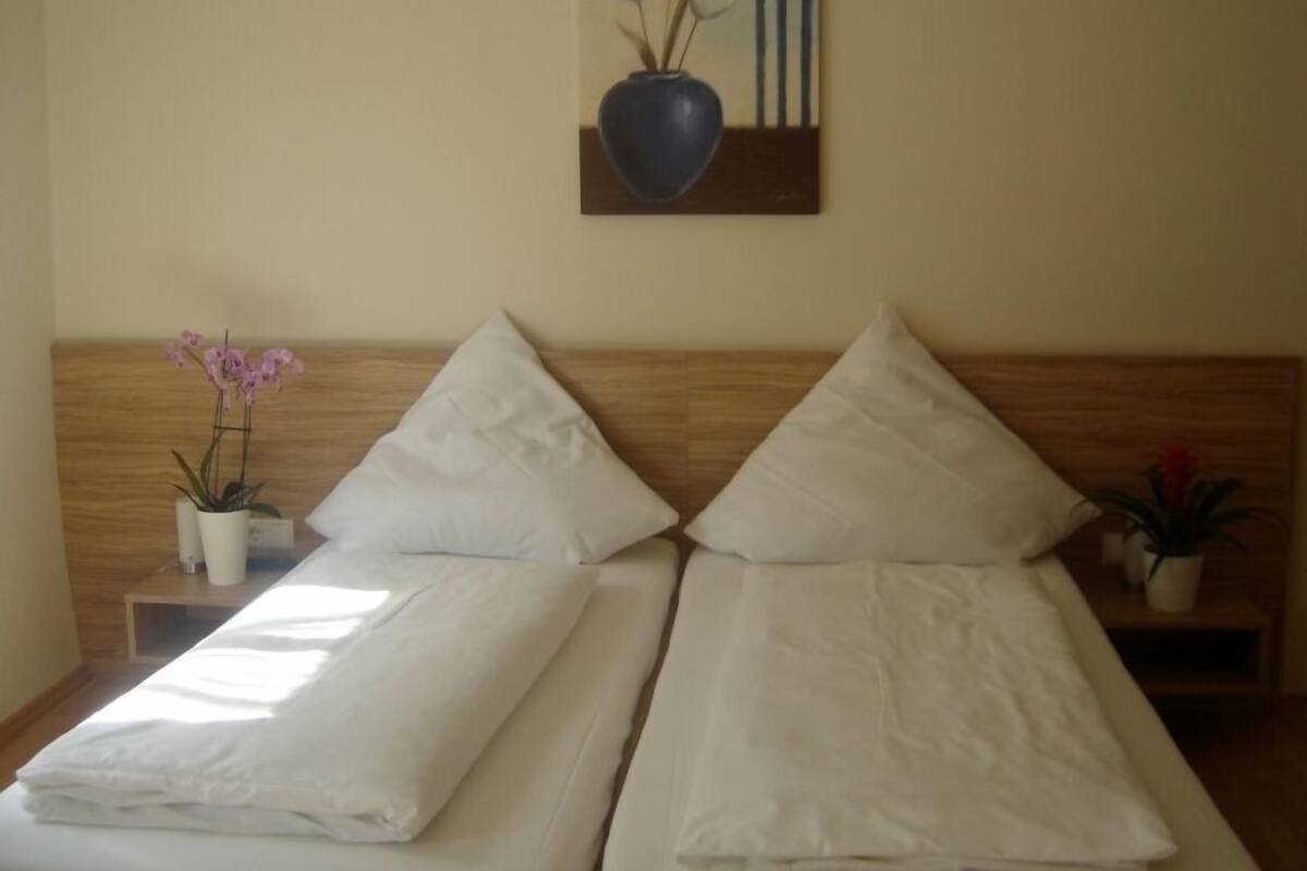 Una cama doble con sábanas blancas, un cabecero de madera y una mesita de noche con una orquídea en maceta.