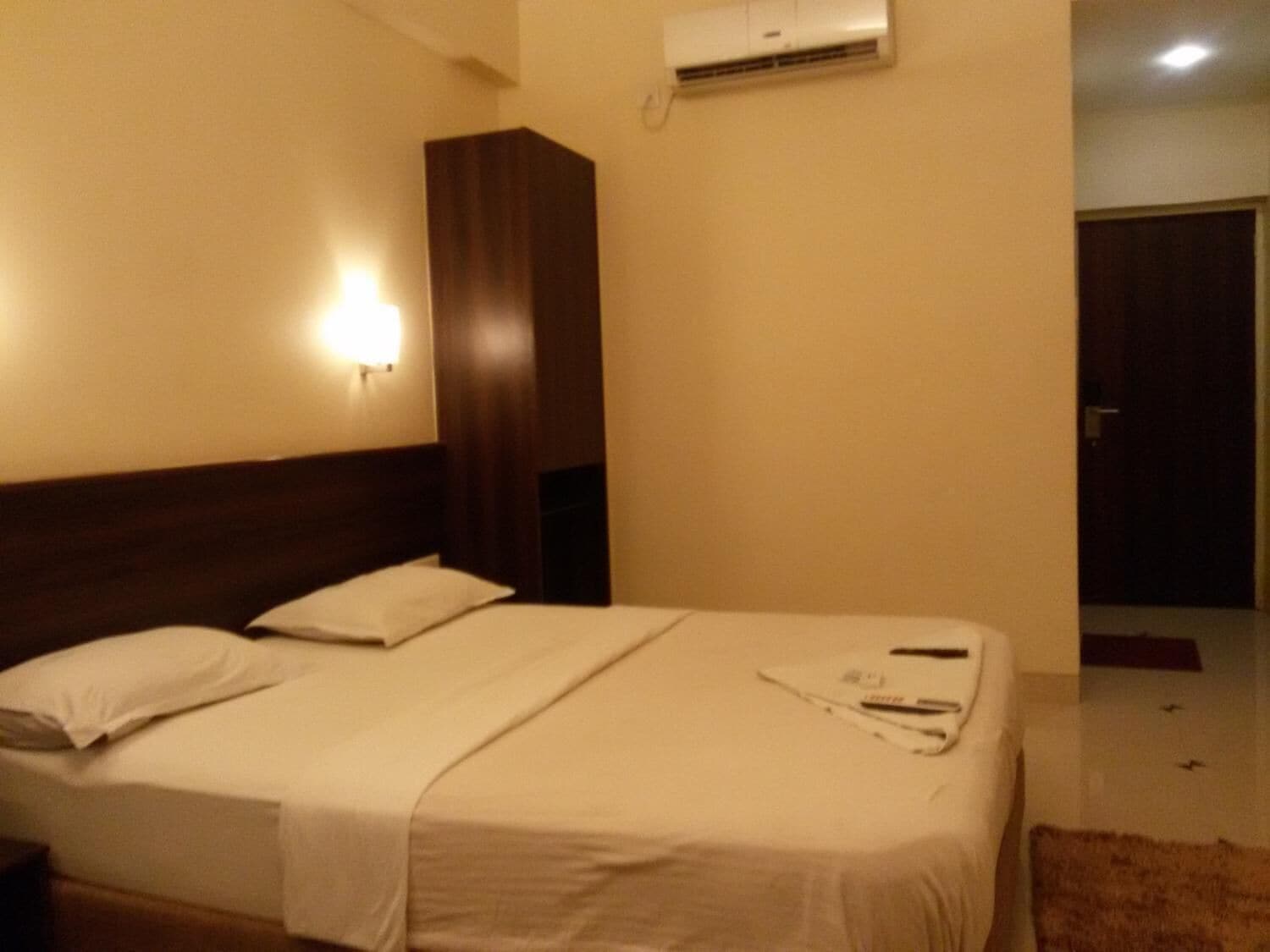 Cama bem arrumada com lençóis brancos, cabeceira de madeira e ar-condicionado fixado na parede.