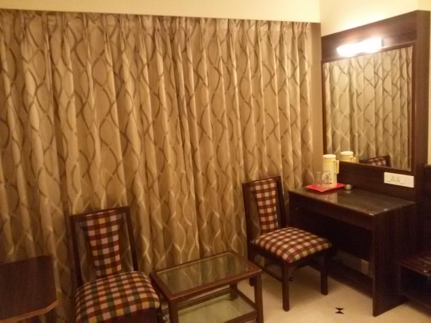 Una habitación de hotel con una silla a cuadros, una mesita pequeña y un espejo en la pared.