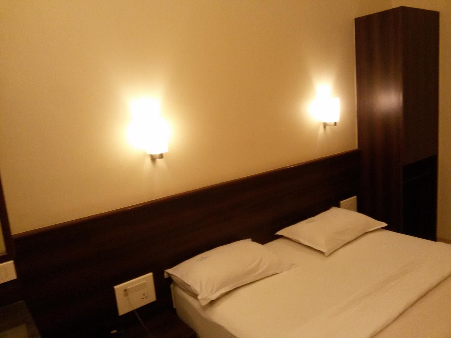 A hotel room with a wooden headboard, two bedside lamps, and a bed with white linens.