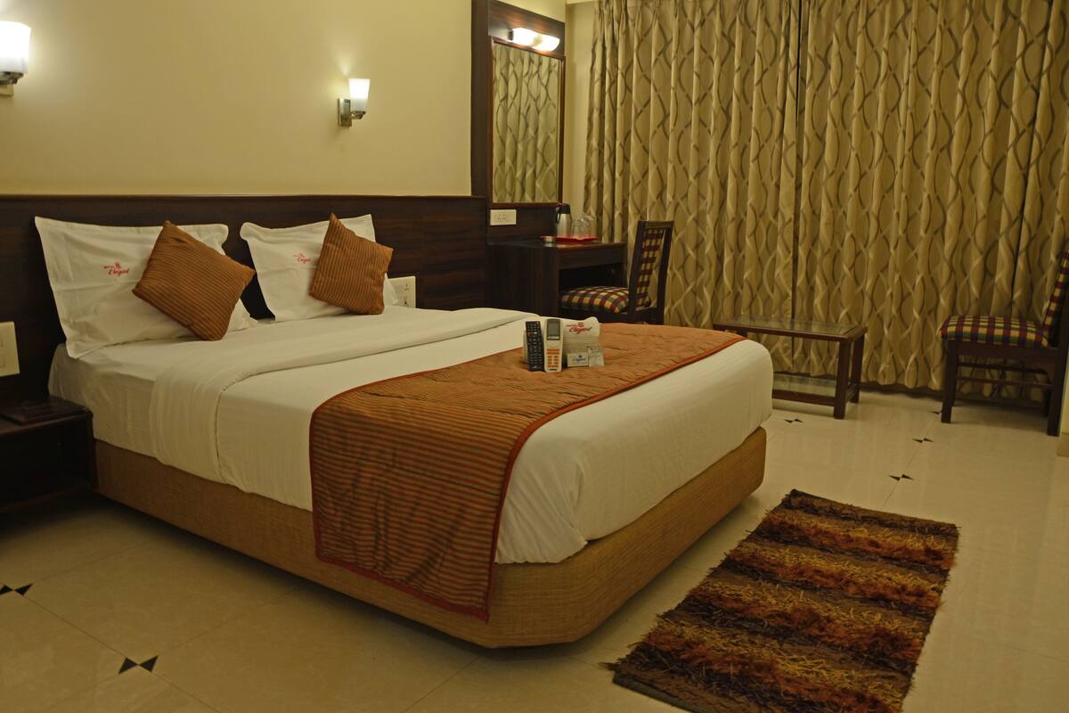 A hotel room with a bed, bedside table, chair, and a mirror.
