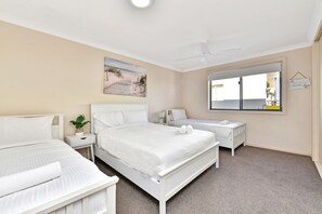 Een hotelkamer met twee bedden, een groot raam, een plafondventilator en een schilderij met een strandthema.