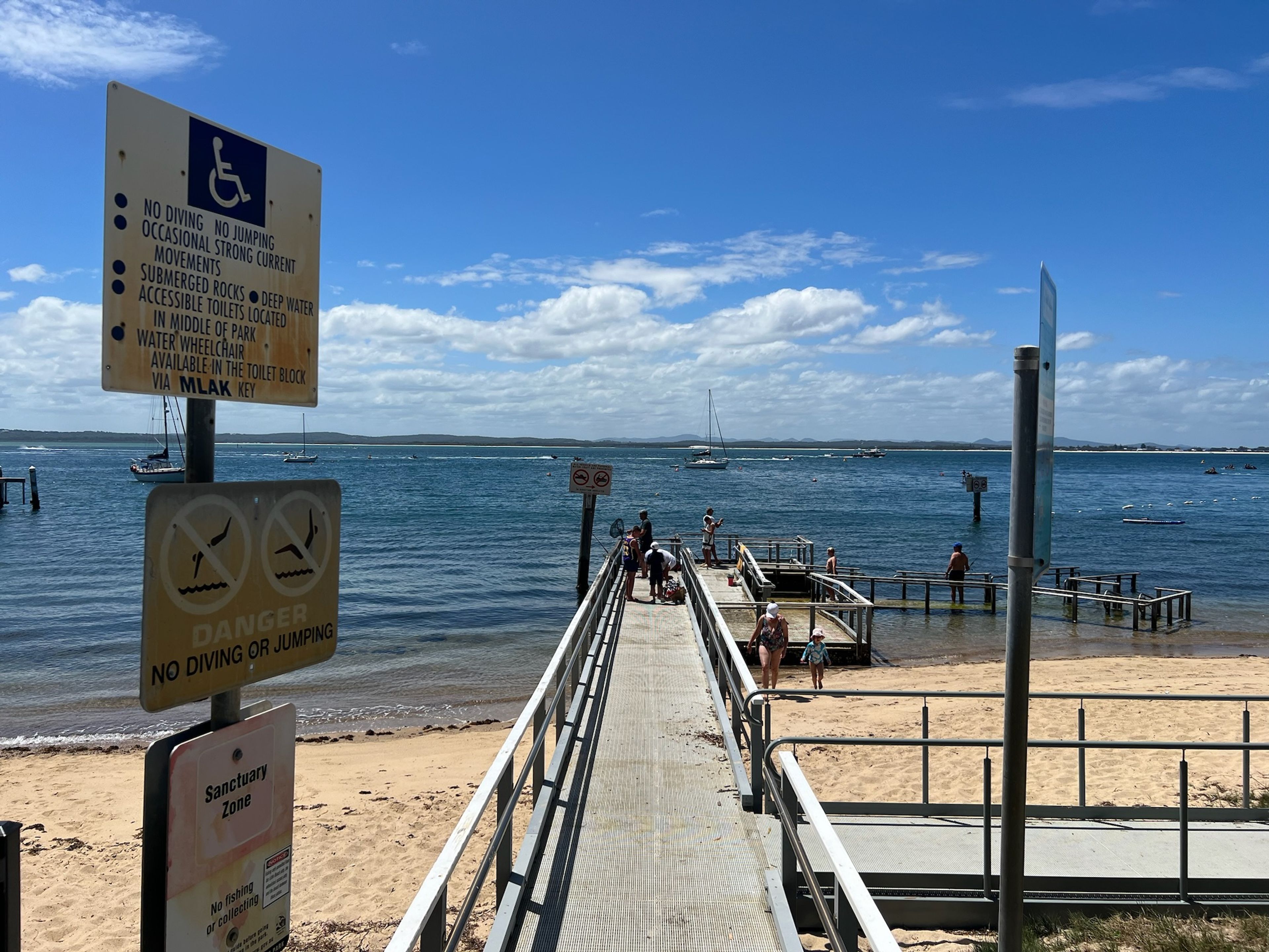 A beach with a pier, signs indicating no diving or jumping, and a sanctuary zone with no fishing.