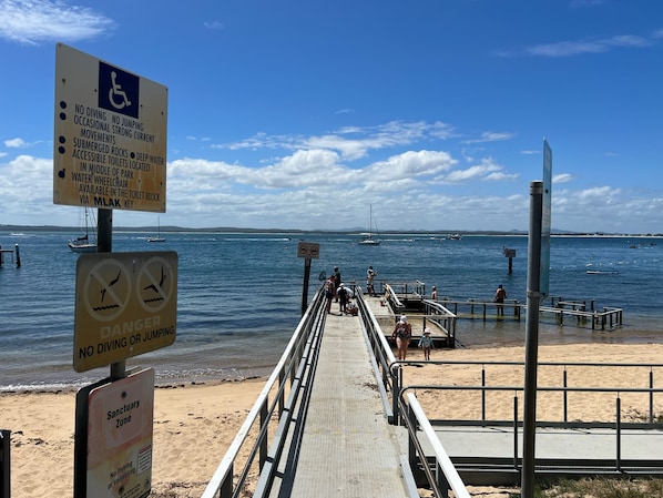 A beach with a pier, signs indicating no diving or jumping, and a sanctuary zone with no fishing.