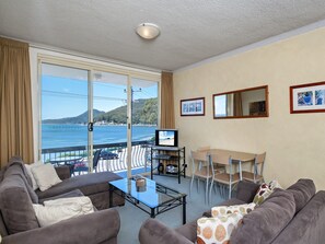 A room with a balcony, a television, a dining table with chairs, and a sofa.