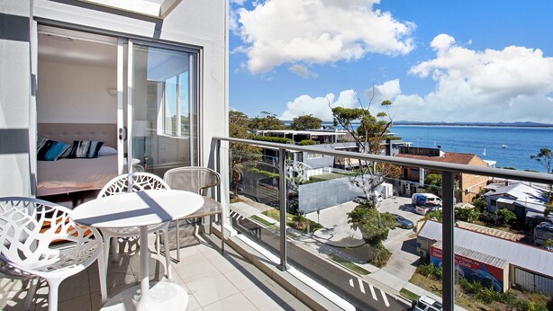 A balcony with a table and chairs, overlooking a coastal area with buildings and a clear sky. - The Shoal 510 panoramic water views (Shoal Bay)