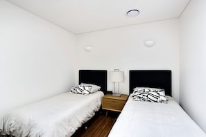 A small, simple room with two single beds, a bedside table with a lamp, and a small drawer. - The Shoal 510 panoramic water views (Shoal Bay)