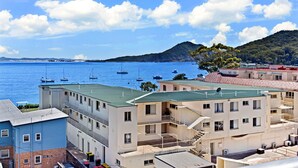 A coastal building with multiple balconies overlooking the sea, a clear sky, and boats in the water. - The Shoal 510 panoramic water views (Shoal Bay)