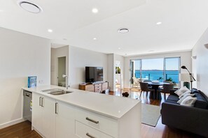 A modern kitchen with a central island, a dining area with a view of the sea, and a cozy seating area with a sofa and a lamp.