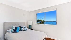 Ein Schlafzimmer mit einem Bett, einem Nachttisch, einer Lampe und einem Fenster mit Meerblick.