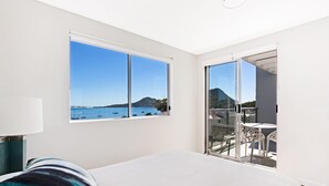 A bedroom with a large bed, a window with a view of the sea, and a balcony with outdoor furniture. - The Shoal 510 panoramic water views (Shoal Bay)