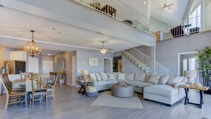 Un vaste espace de vie comprenant un grand canapé d’angle, une table à manger avec des chaises et un escalier menant à un niveau supérieur.