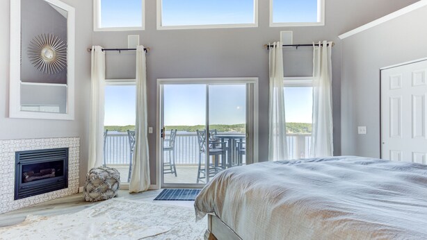 Une chambre avec un grand lit, une cheminée et un balcon offrant une vue sur l’eau.