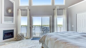 Een slaapkamer met een groot bed, een open haard en een balkon met uitzicht op het water.