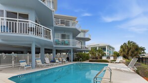 A swimming pool with lounge chairs and a multi-story building with balconies. - Amadeus 3 Amazing Water view|Steps to beach|Top location! (Treasure Island)