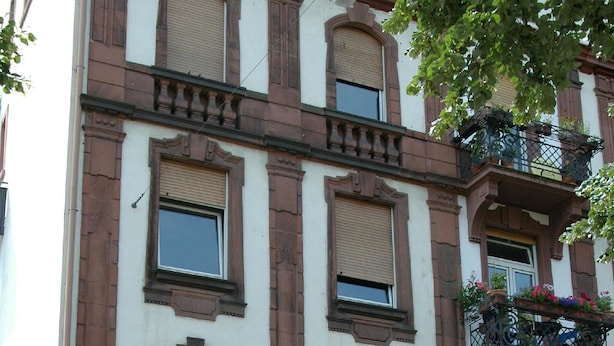 Ein mehrgeschossiges Gebäude im klassischen Stil, mit Bogenfenstern und einem Balkon mit Blumentöpfen.