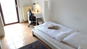 Ein Schlafzimmer mit Bett, Schreibtisch, Stuhl, Lampe und Heizkörper.