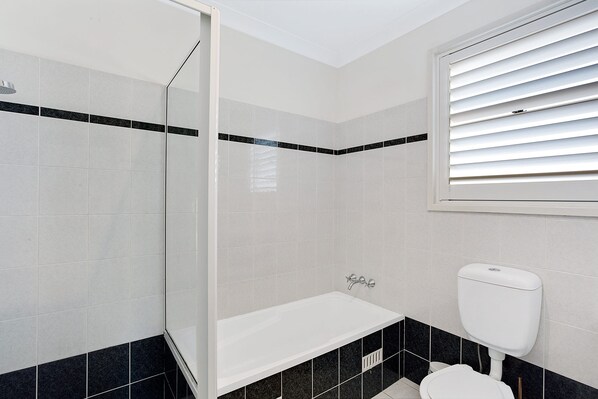 Une salle de bain avec douche, toilettes et une fenêtre équipée de stores.