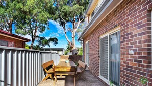 A patio with a wooden table and chairs, a brick wall, and a metal fence. - Sandy Shores 1 Pet Friendly Shoal Bay Home (Shoal Bay)