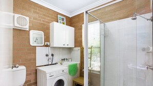 A compact bathroom with a washing machine, a toilet, a shower, and a small sink. - Sandy Shores 1 Pet Friendly Shoal Bay Home (Shoal Bay)