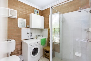 Een compacte badkamer met een wasmachine, toilet, douche en een klein wastafeltje.