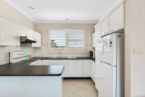 A kitchen with white cabinets, a black countertop, a microwave, and a refrigerator.