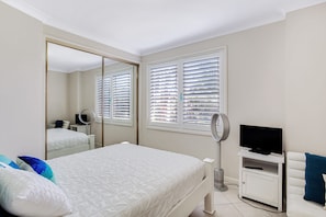 Een slaapkamer met een bed, een televisie, een spiegel en een raam met zonwering.
