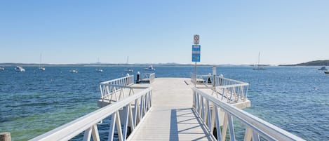 A pier leading into calm waters with boats and a clear sky.