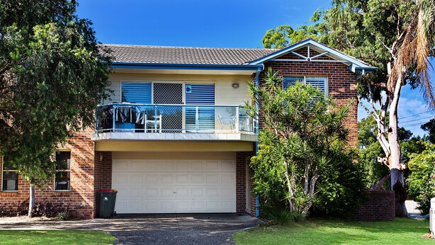 A two-story house with a garage, a balcony, and a driveway leading to the garage. - Sandy Shores 1 Pet Friendly Shoal Bay Home (Shoal Bay)