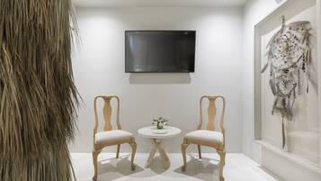 A room with two wooden chairs, a small round table with a vase, a mounted flat-screen TV, and a wall-mounted artwork.