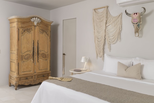 Une chambre avec une grande armoire en bois, un lit avec une literie blanche, une décoration murale en macramé et un crâne de taureau décoratif.
