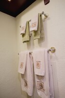 Un baño con dos barras para toallas que sostienen tres toallas, una verde y dos rosas, con bordados.