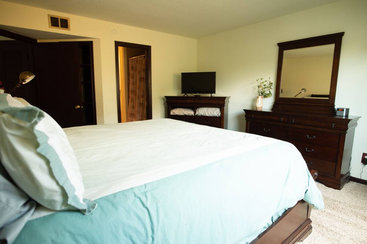 A bedroom with a large bed, a dresser, a television, and a mirror.