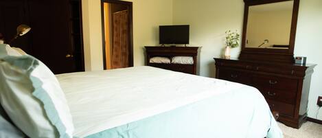 A bedroom with a large bed, a dresser, a television, and a mirror.