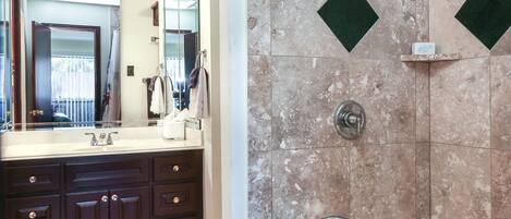 A bathroom with a marble shower wall, a large mirror, and a bathtub.