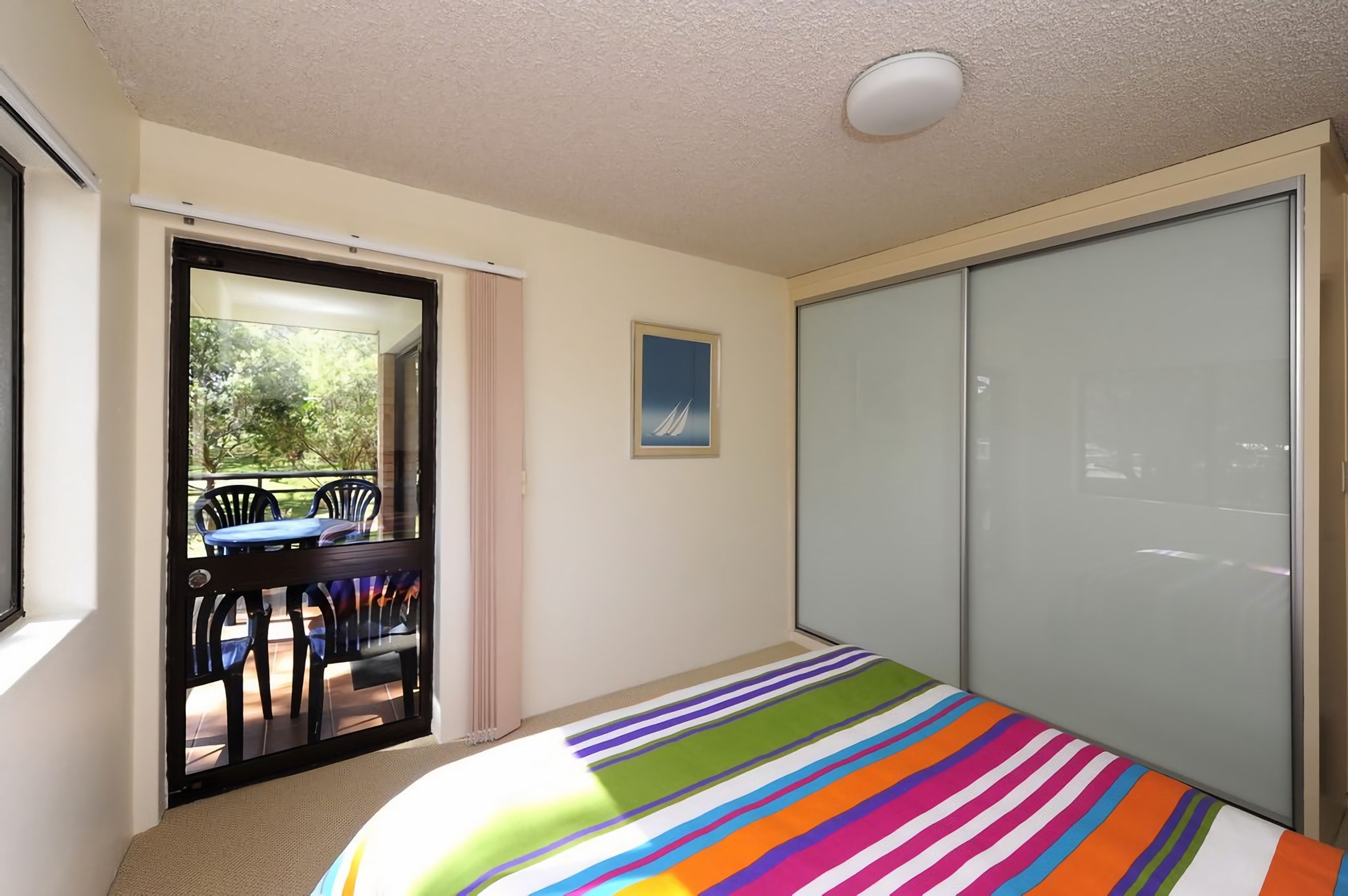Un dormitorio con una cama, una puerta corredera a un balcón y un cuadro en la pared.
