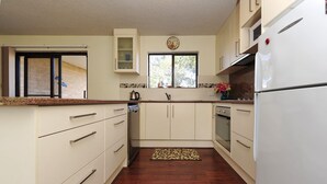 A kitchen with white cabinets, a refrigerator, a stove, and a window with a view of trees. - Shoreline 2 Retreat Near Nelson Bay Beach (Nelson Bay)