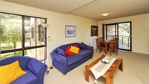 A living room with a blue sofa, a wooden coffee table, and a dining area with a table and chairs. - Shoreline 2 Retreat Near Nelson Bay Beach (Nelson Bay)