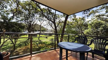 A balcony with a table and chairs, overlooking a grassy area with trees and a distant building.
