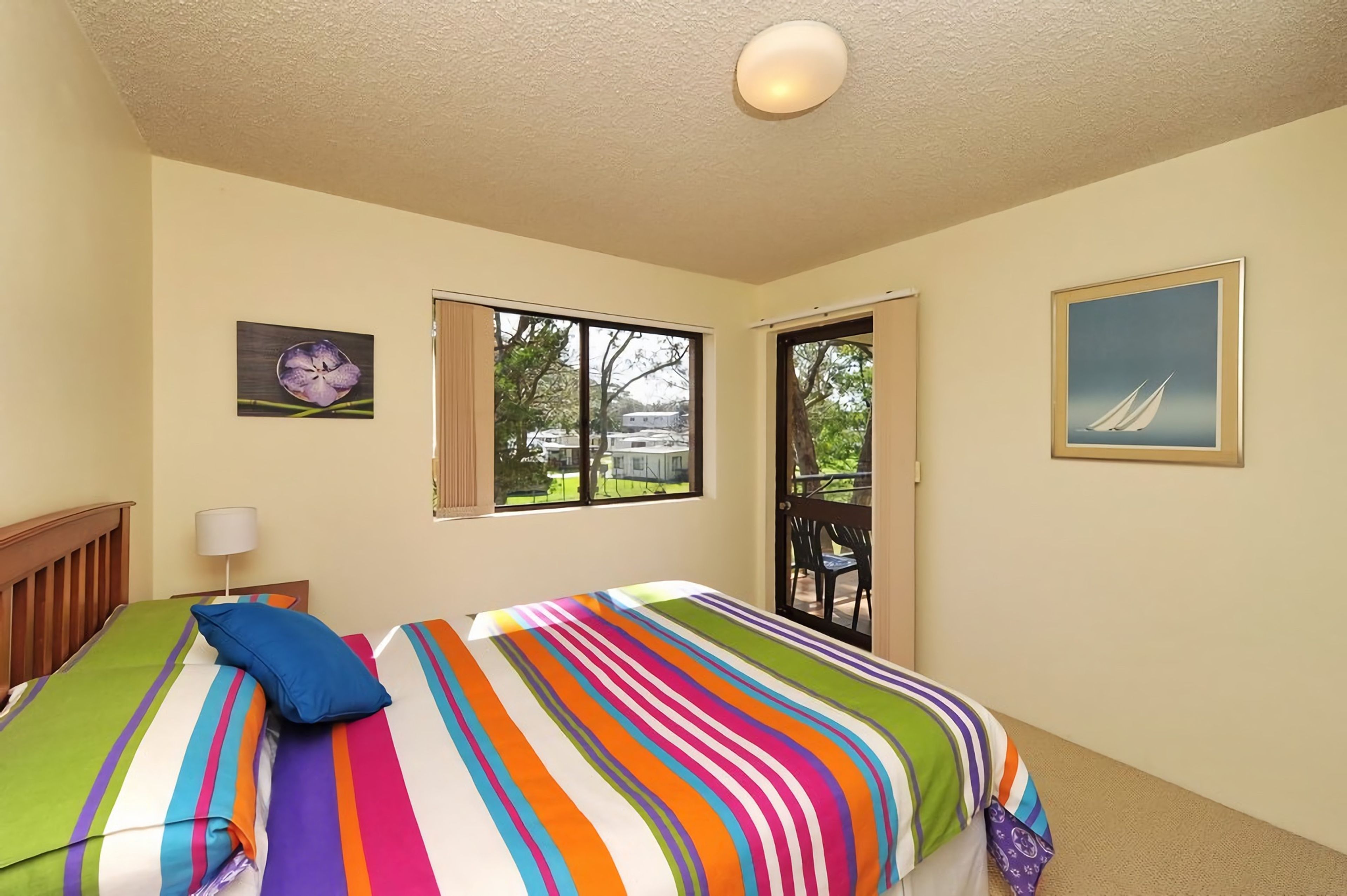 A bedroom with a bed, a window, a door, and a painting on the wall.