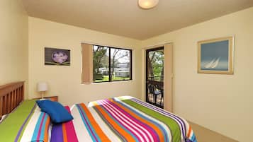 A bedroom with a bed, a window, a door, and a painting on the wall.