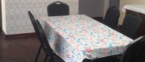 Un salón de conferencias con una mesa cubierta con mantel floral, rodeada de sillas negras. Un televisor montado en la pared muestra un evento deportivo.