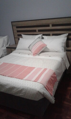 Una cama con cabecera de madera, ropa de cama blanca y una manta rayada rosa.