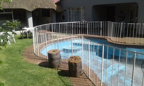 Una piscina con valla metálica blanca, rodeada por un suelo de ladrillo y césped.
