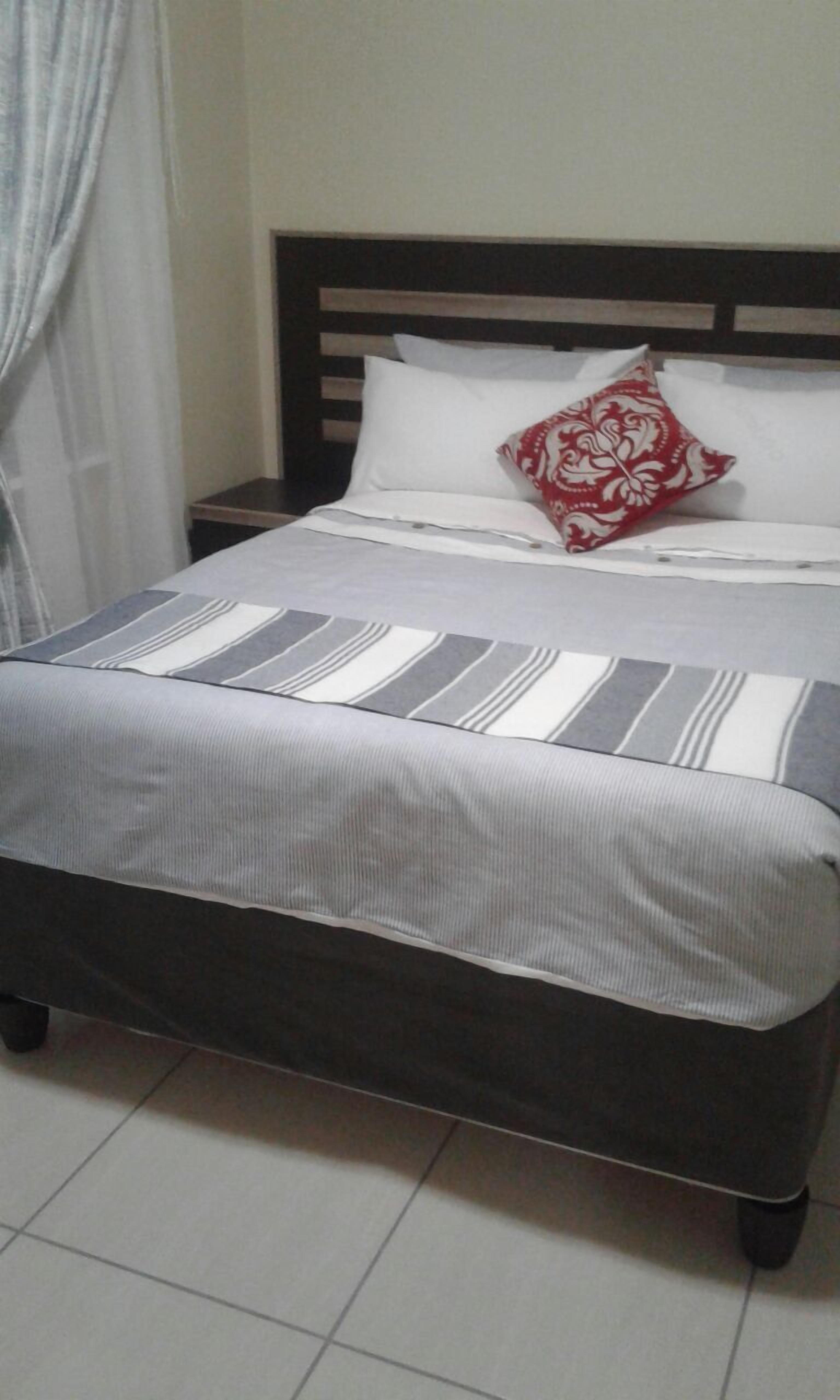 Una cama con una colcha a rayas, un cabecero de madera y una mesita de noche con una lámpara.