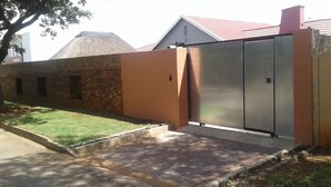 A gated property with a brick wall, a paved driveway, and a metal gate. - Acacia Guesthouse (Kempton Park)